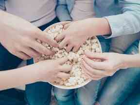 Vue de dessus portrait en gros plan de mains prenant du maïs soufflé sucré dans un seau, papa maman enfants partageant du pop-corn tout en regardant un programme télévisé, assis sur un canapé à l'intérieur, profitant du temps libre en s'amusant