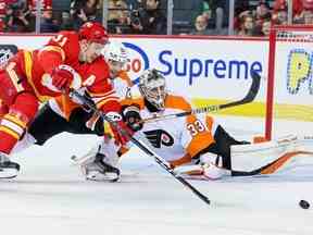 L'attaquant des Flames de Calgary Mikael Backlund et l'attaquant des Flyers de Philadelphie Scott Laughton se battent pour la rondelle devant le gardien des Flyers Samuel Ersson au Scotiabank Saddledome de Calgary le lundi 20 février 2023.