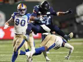 Le demi offensif des Argonauts de Toronto Andrew Harris (33) survole le demi défensif des Blue Bombers de Winnipeg Brandon Alexander (37) sous le regard du plaqueur défensif Casey Sayles (90) lors de la 109e Coupe Grey au stade Mosaic de Regina, le dimanche 20 novembre 2022. Harris a accepté une prolongation de contrat d'un an avec les Argonauts, selon une source de la LCF.