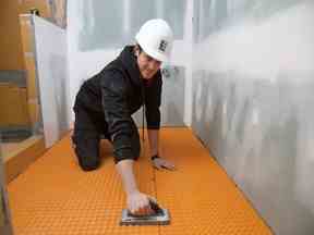 Michael installe une membrane de découplage dans le cadre du système de chauffage électrique intégré au sol dans une récente rénovation de salle de bain.