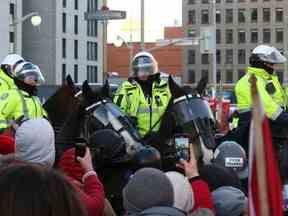 Des manifestants se tiennent devant des policiers canadiens à cheval, alors que des camionneurs et des partisans protestent contre les mandats de vaccination contre la COVID-19, à Ottawa, le 18 février 2022.