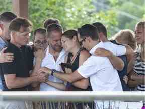 Amélie Lemieux, au centre, est réconfortée par des membres de sa famille alors qu'elle tient des photos de ses deux filles, Romy et Norah Carpentier, lors d'un mémorial à Lévis le 13 juillet 2020.