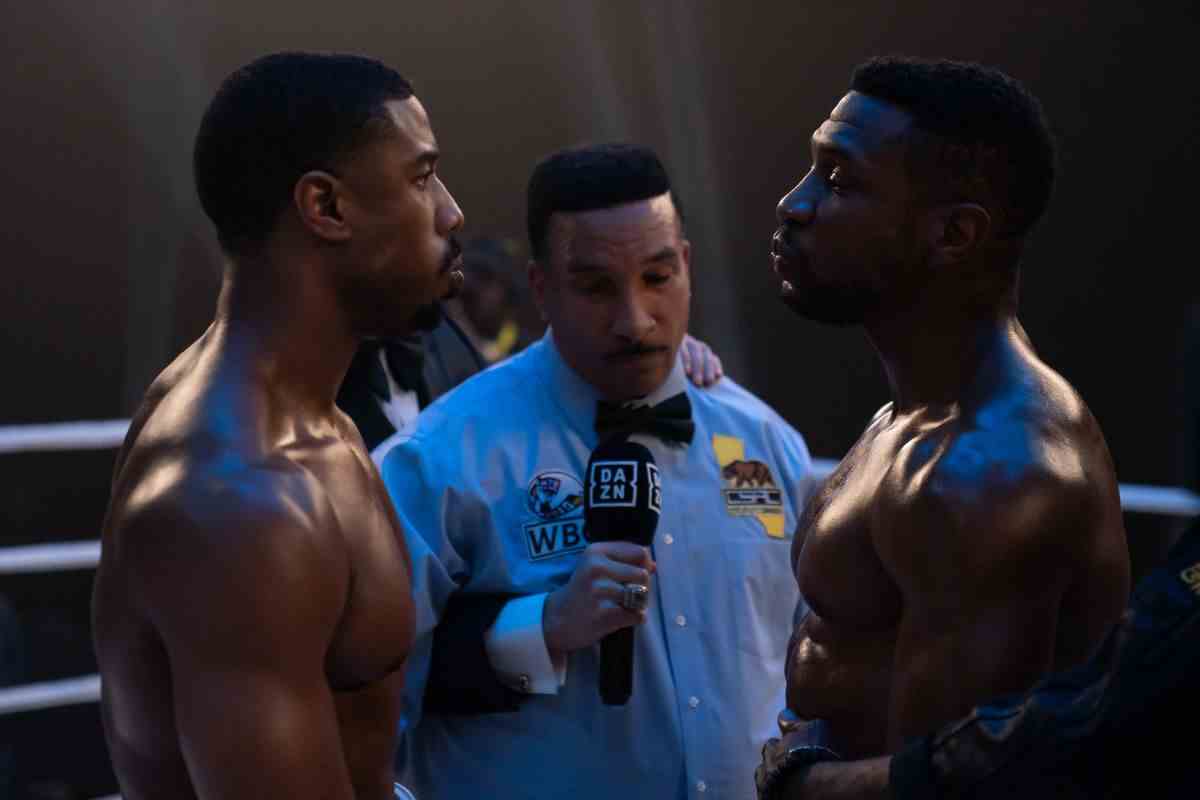 Adonis Creed (Michael B Jordan) et Damian (Jonathan Majors) se tiennent torse nu l'un en face de l'autre avec un arbitre de boxe au milieu prêt à se battre dans Creed III