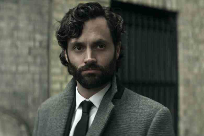 A man with dark hair and a beard wearing a gray suit and black tie; still of Penn Badgley in "You"