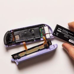 Retirez délicatement la batterie et essayez de garder son adhésif sans poussière afin qu'il conserve une certaine adhérence lorsque vous réinsérez la batterie plus tard.  Ensuite, dévissez le cache en plastique noir maintenu par deux vis de type J00.  Rangez-les soigneusement, puis soulevez le plastique pour révéler la carte principale.