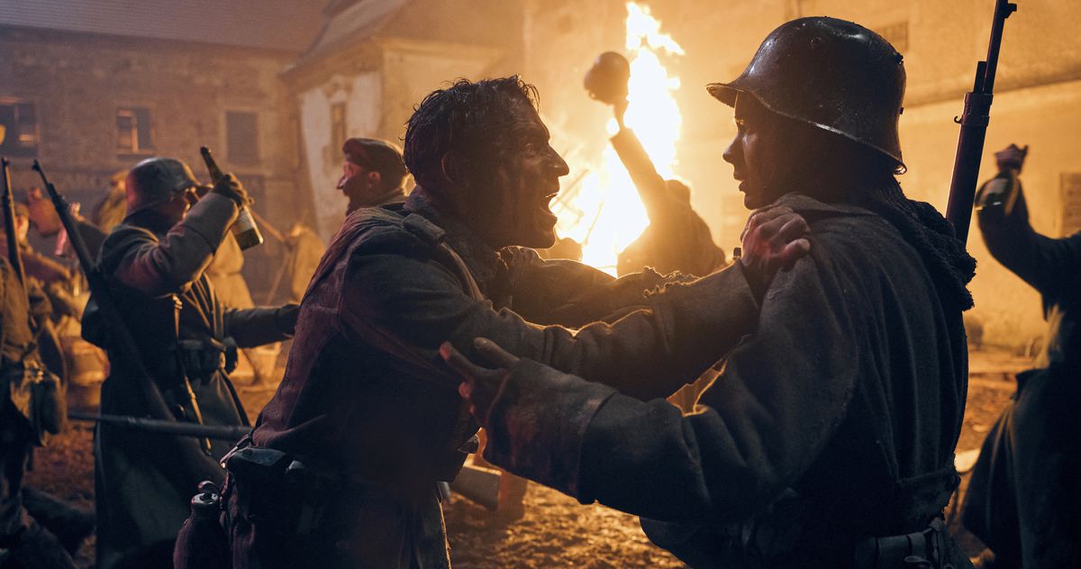 Un soldat sans casque, le visage maculé de sang, crie au visage d'un autre alors qu'une célébration éclate dans une rue de la ville la nuit devant un incendie qui se propage dans le nominé du meilleur film de Netflix All Quiet on the Western Front