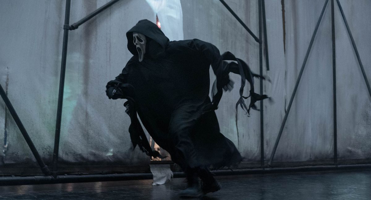 Ghostface, le tueur à la robe noire et au masque blanc de la franchise Scream, court après quelqu'un sur fond de canevas blancs retenus par un échafaudage noir dans Scream VI