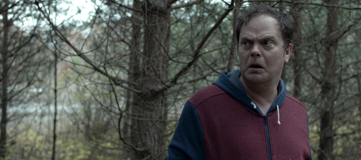 Rainn Wilson debout dans une forêt, l'air perplexe devant le lac Shimmer de 2017