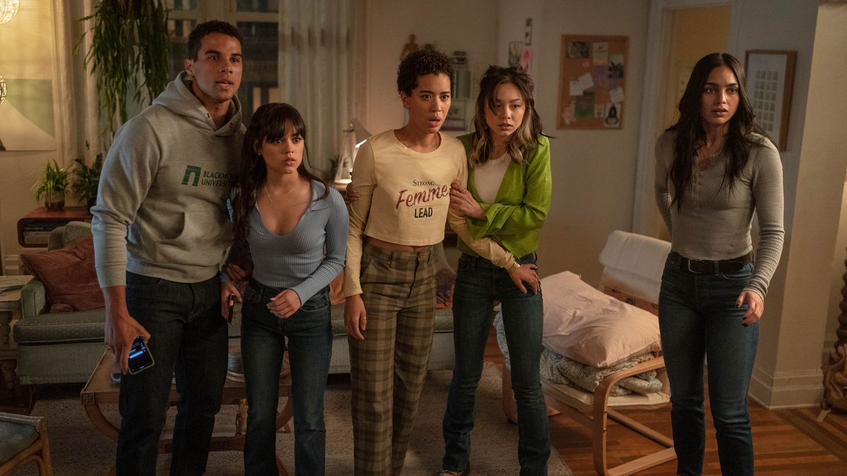 Cinq membres de la distribution de Scream VI (Devyn Nekoda, Jasmin Savoy Brown, Jenna Ortega, Mason Gooding, Melissa Barrera) se tiennent ensemble dans un salon, se serrent les uns les autres pour se soutenir et regardent quelque chose hors écran dans Scream VI