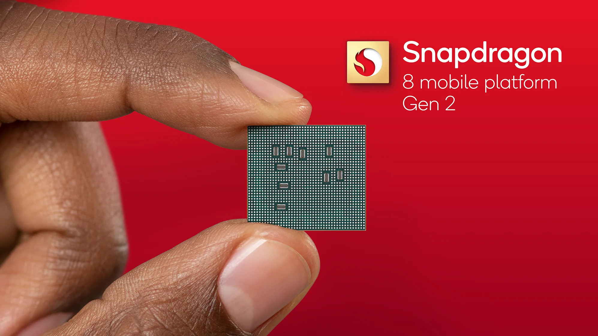 Image de doigts tenant une puce Qualcomm Snapdragon 8 Gen 2 sur fond rouge