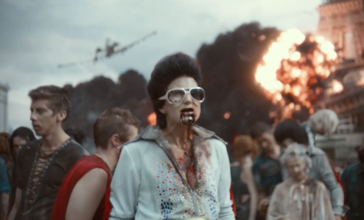 Un imitateur d'Elvis zombie se promène dans Vegas avec d'autres zombies alors qu'une explosion se produit derrière eux dans Army of the Dead.