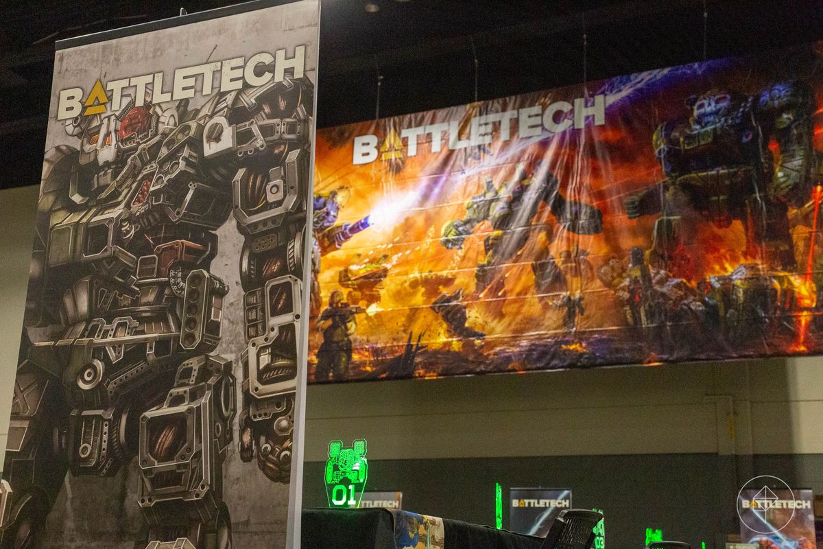 Un standee d'un Atlas 'mech, son crâne blindé dominant l'image.  En arrière-plan, l'illustration complète du coffret BattleTech.