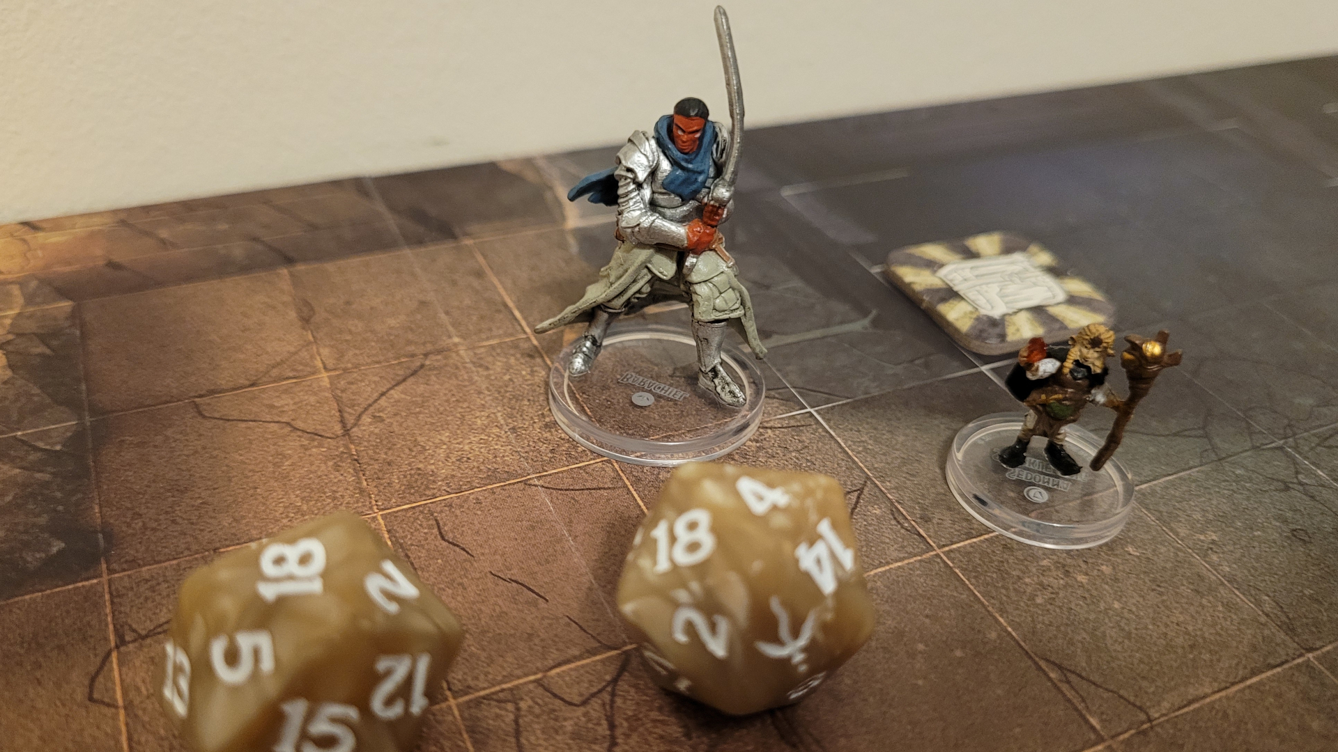 Un modèle d'un guerrier brandissant une épée se tient devant deux dés et sur un plateau de Dungeons & Dragons : Onslaught