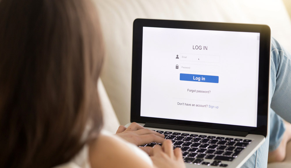 Une femme utilisant un ordinateur portable allongée sur un canapé, avec un écran de connexion à un site Web affiché sur l'ordinateur portable.