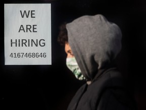 Un piéton portant un masque devant une pancarte annonçant l'embauche à Toronto.