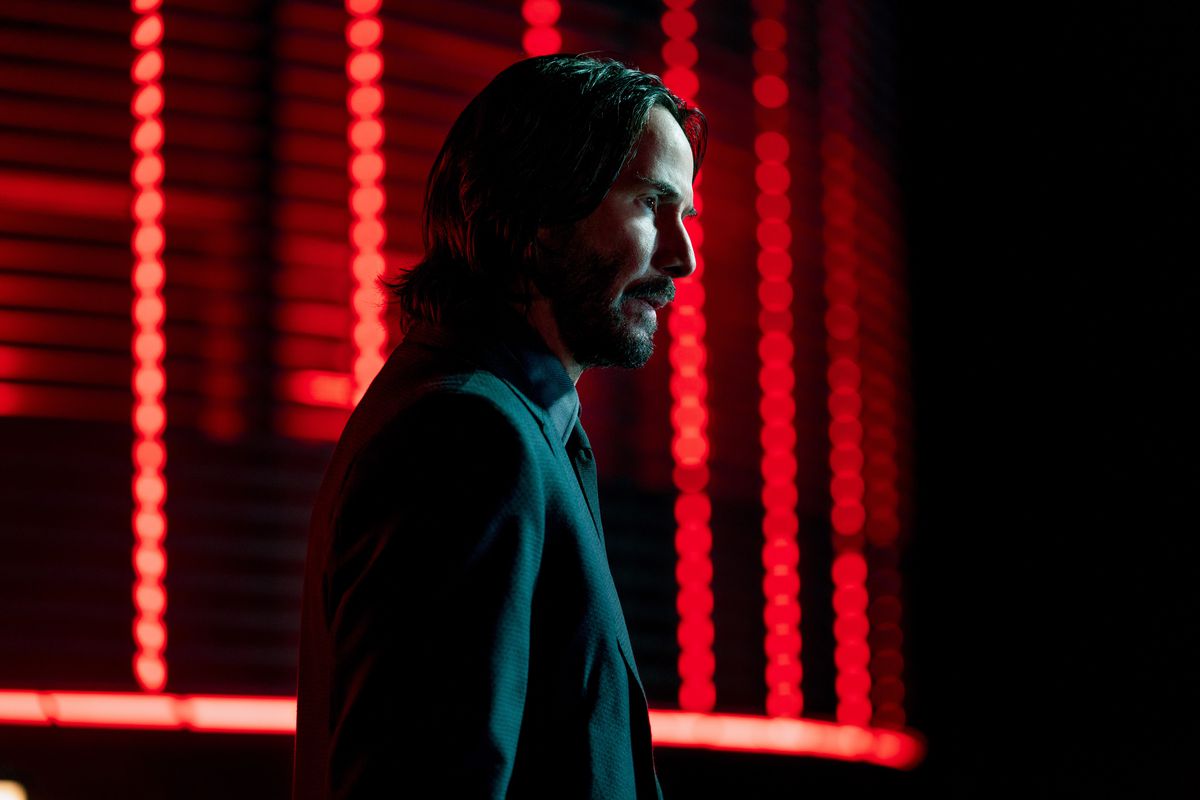 Un plan moyen de John Wick debout devant des néons rouges dans John Wick: Chapitre 4