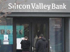 Les gens regardent les panneaux affichés à l'extérieur d'une entrée de la Silicon Valley Bank à Santa Clara, en Californie, le vendredi 10 mars 2023. La Federal Deposit Insurance Corporation saisit les actifs de la Silicon Valley Bank, marquant la plus grande faillite bancaire depuis Washington Mutual pendant au plus fort de la crise financière de 2008.  La FDIC a ordonné la fermeture de la Silicon Valley Bank et a immédiatement pris position sur tous les dépôts à la banque vendredi.