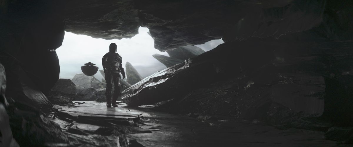 Mandalorian (Pedro Pascal) et Grogu entrant dans une grotte.  Grogu est dans son pod en vol stationnaire