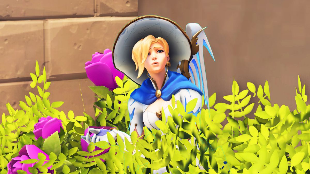 Mercy from Overwatch hiding in a bush. She is shrugging. She seems confused.