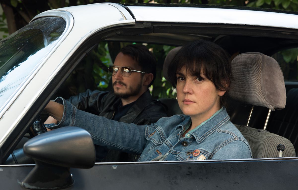 (LR) Elijah Wood et Melanie Lynskey assis au volant d'une voiture dans Je ne me sens plus chez moi dans ce monde