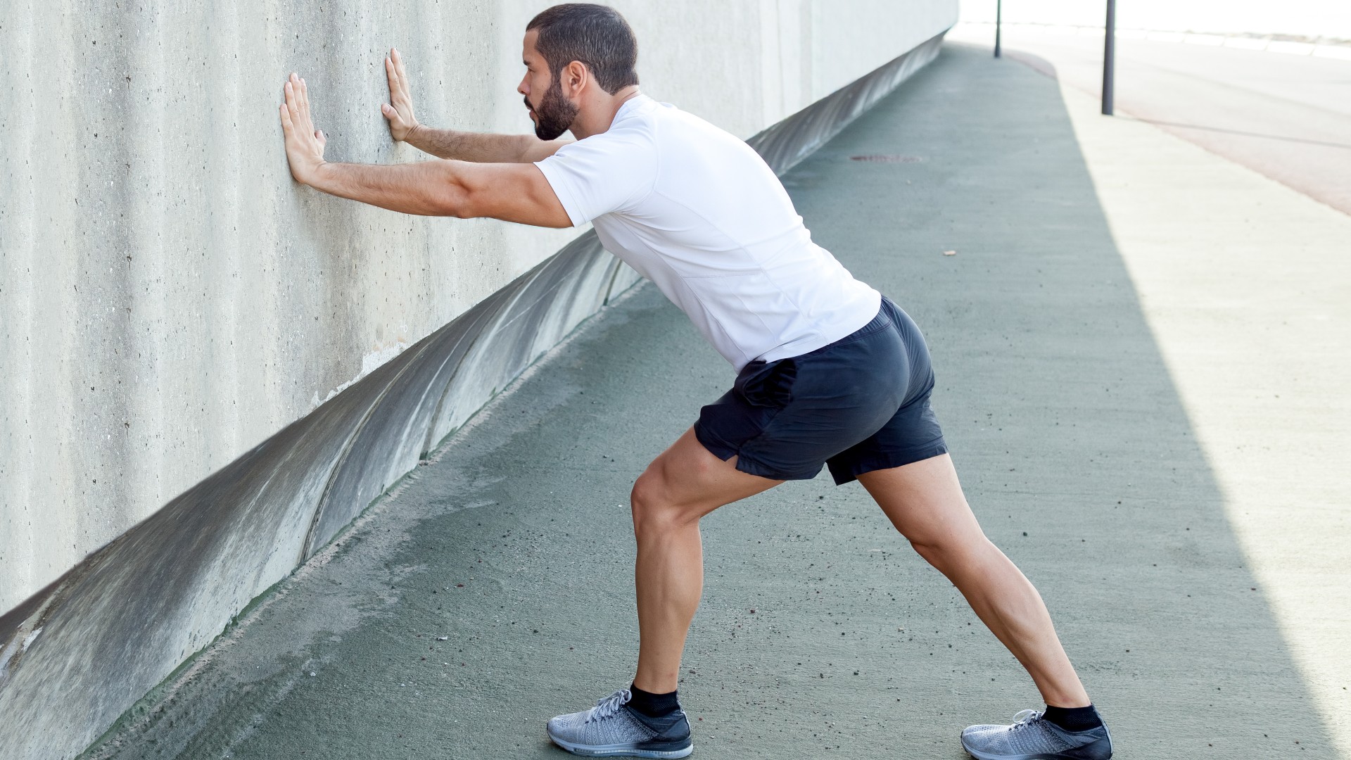 Homme avec les bras appuyés sur un mur jambe gauche en avant et jambe droite en arrière