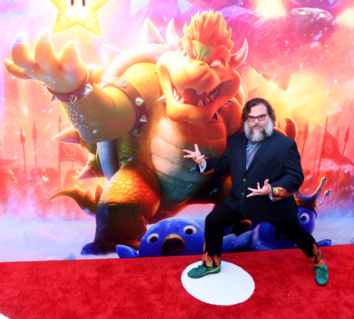 Jack Black pose, avec des mains en forme de griffes, sur le tapis rouge lors de la première à Los Angeles du film Super Mario Bros.  Il porte un costume avec des pointes dans le dos de Bowser et une chemise avec un imprimé holographique d'écailles de lézard.