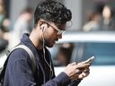 Un homme traverse la rue Dundas à la hauteur de la rue Yonge à Toronto en utilisant son téléphone cellulaire.