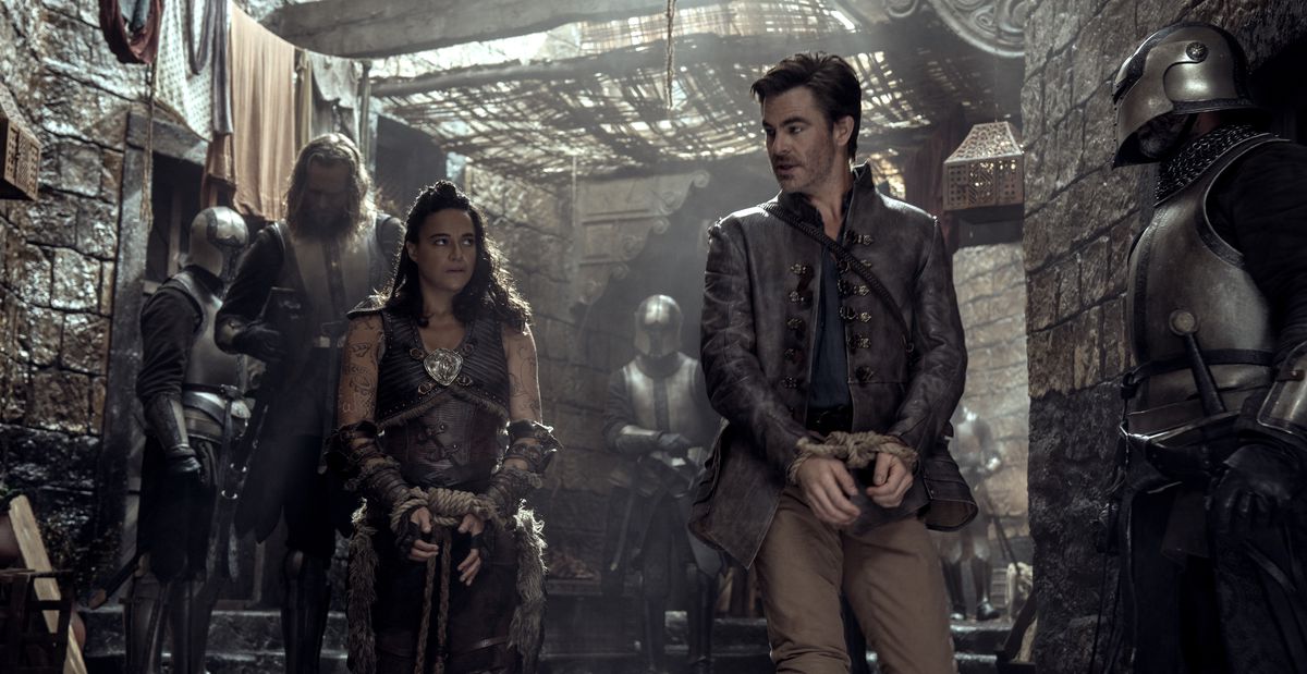 Holga le barbare (Michelle Rodriguez) et Edgin le barde (Chris Pine), menottés et escortés par des gardes, échangent un regard significatif sur le point de s'échapper alors qu'ils marchent dans les rues de Neverwinter dans Dungeons &  Dragons : Honneur parmi les voleurs