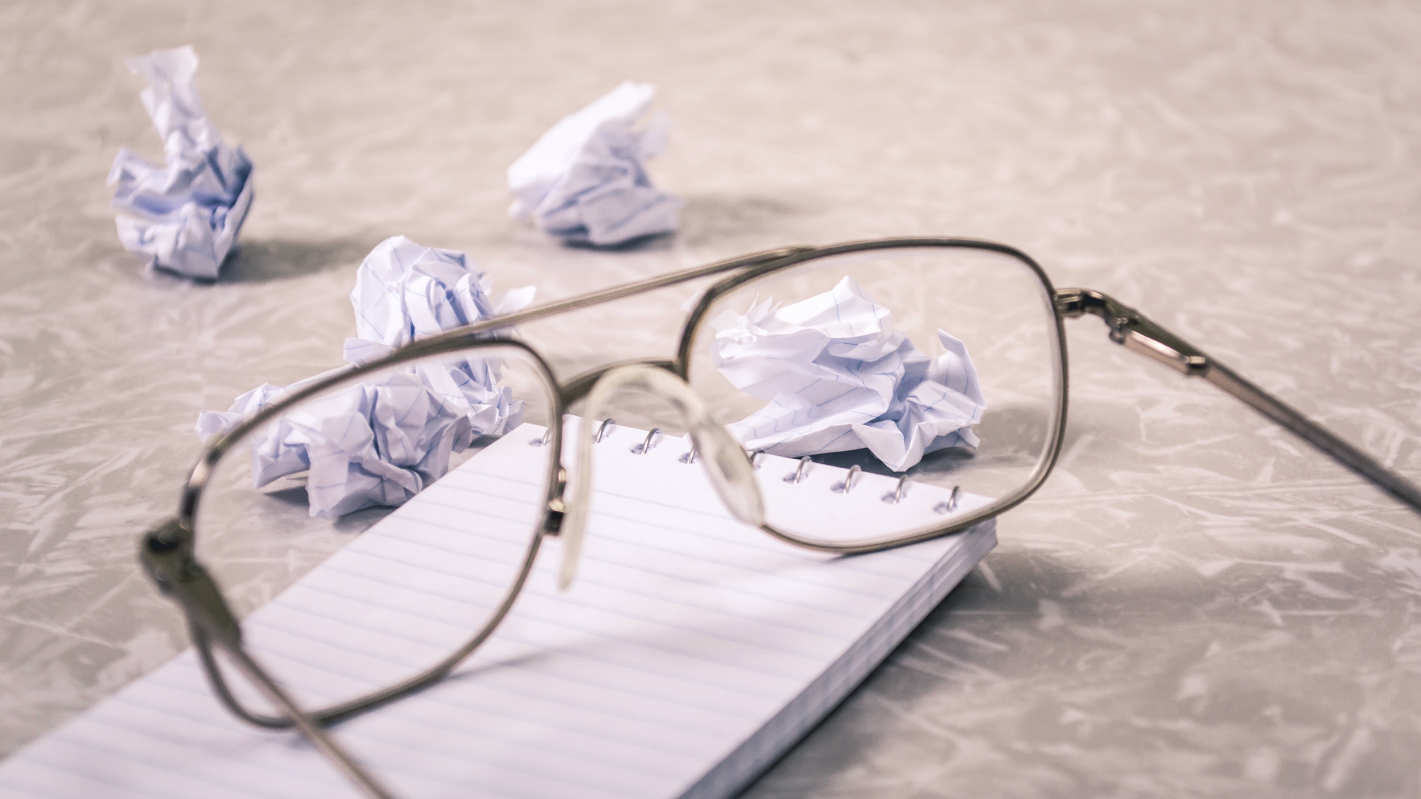 une paire de verre posée sur un cahier.  Sur les côtés se trouvent des morceaux de papier de cahier jetés