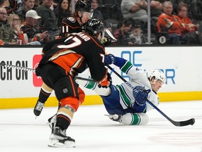 Le centre des Canucks de Vancouver Sheldon Dries, à droite, tombe sous la pression du centre des Ducks d'Anaheim Trevor Zegras, à gauche, et de l'ailier droit Frank Vatrano pendant la première période le mardi 11 avril 2023 à Anaheim, en Californie.