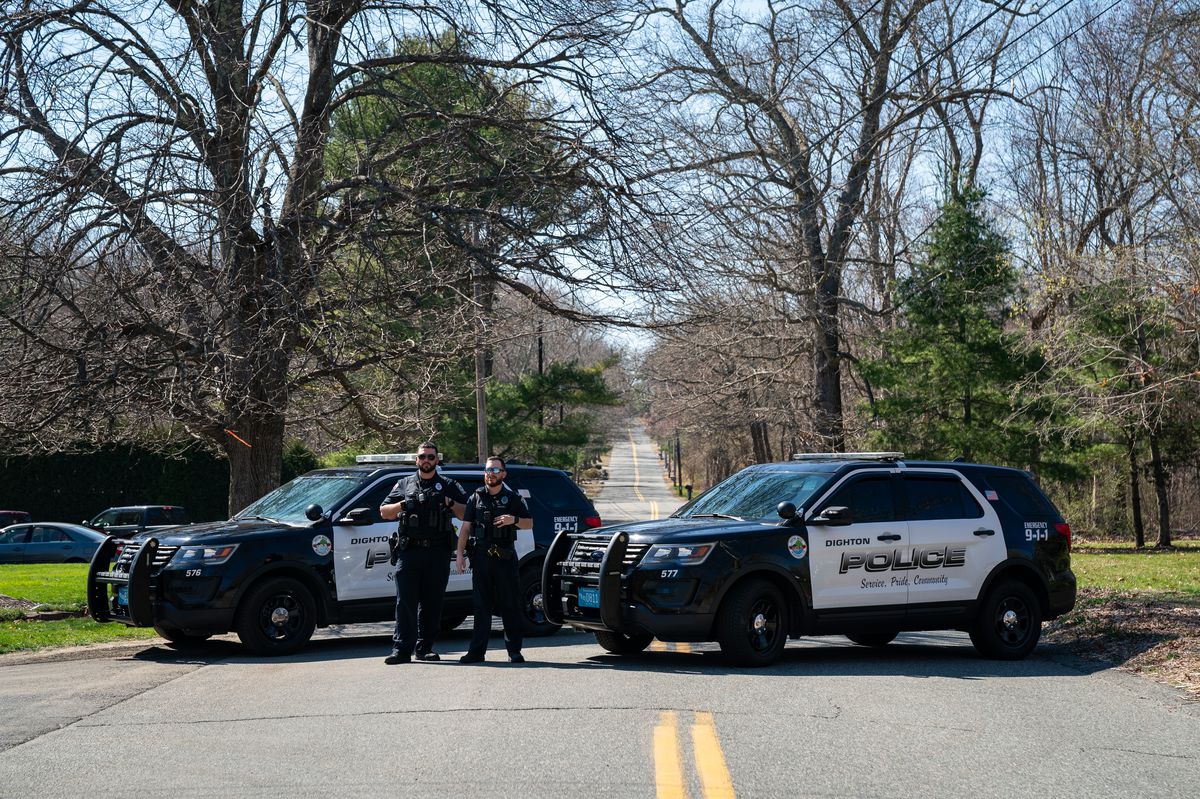 Deux voitures de police bloquent une route à deux voies.  Deux policiers se tiennent devant les véhicules.