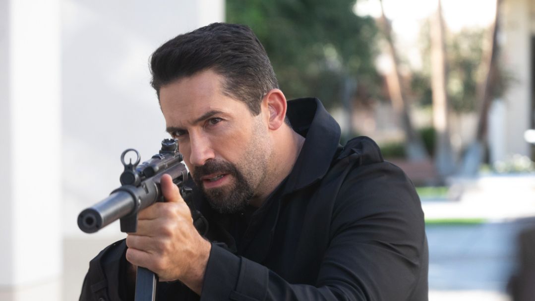 Scott Adkins - un homme avec une barbichette et un manteau noir - visant un fusil dans la section 8.