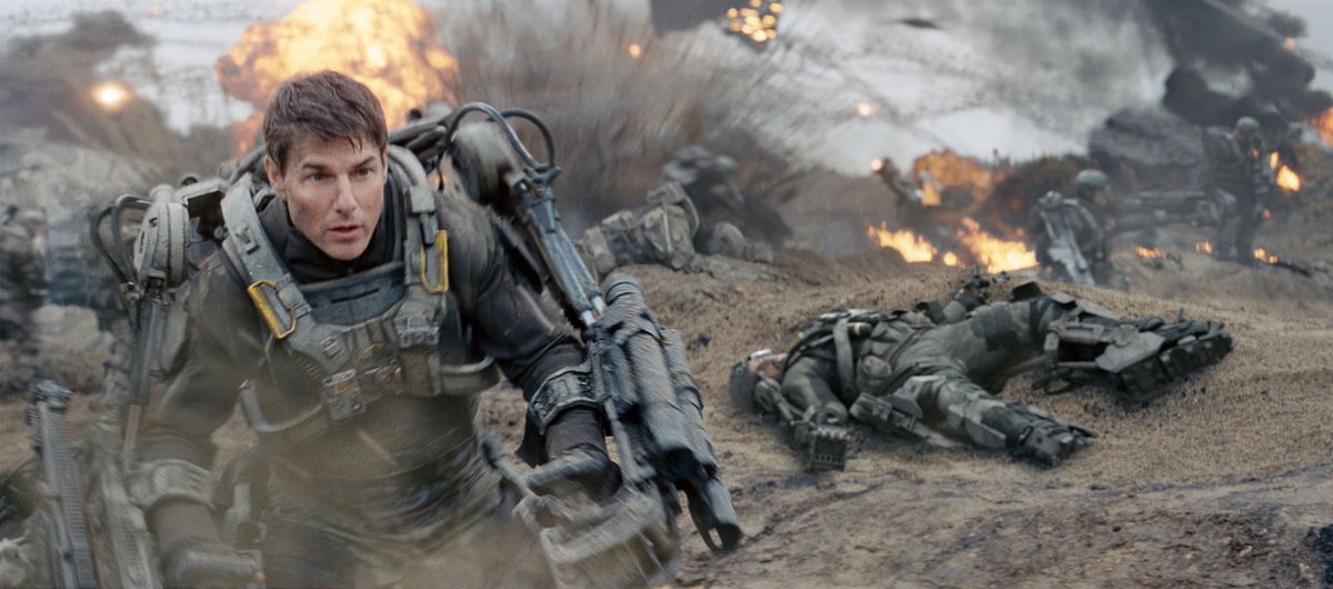 Tom Cruise dans le rôle de Cage en armure assistée prenant d'assaut une plage remplie d'explosions dans Edge of Tomorrow.