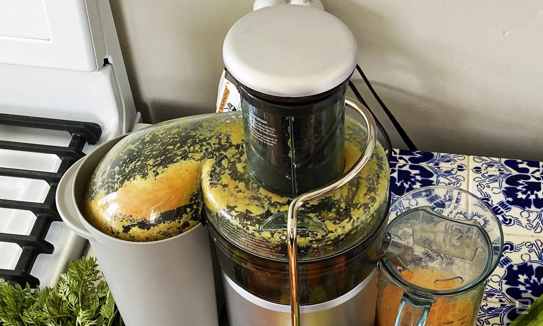 La fontaine à jus Breville plus se trouve sur un comptoir.  Il vient d'être utilisé pour faire une boisson à l'orange à partir de carottes et d'oranges.  Beaucoup de pulpe recouvre le dôme intérieur de l'extracteur de jus. 