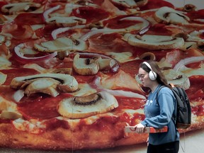 Un piéton passe devant une murale publicitaire de pizza à Toronto.  Pizza Pizza, la plus grande chaîne de pizzas au Canada, s'étend au Mexique.