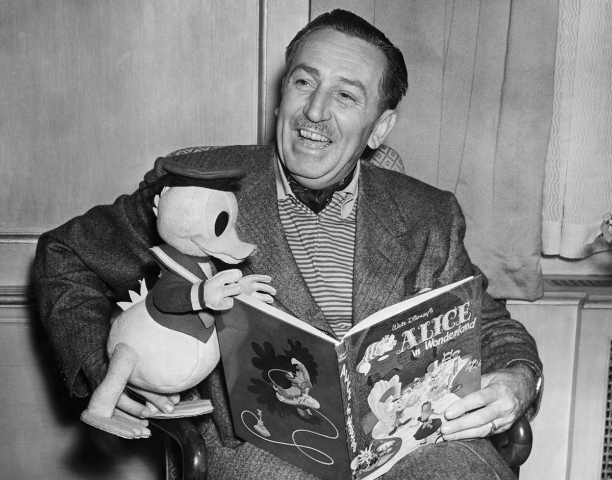 Dans un portrait en noir et blanc de 1951, Walt Disney tient un Donald Duck en peluche sur ses genoux alors qu'il lit une copie d'Alice au pays des merveilles