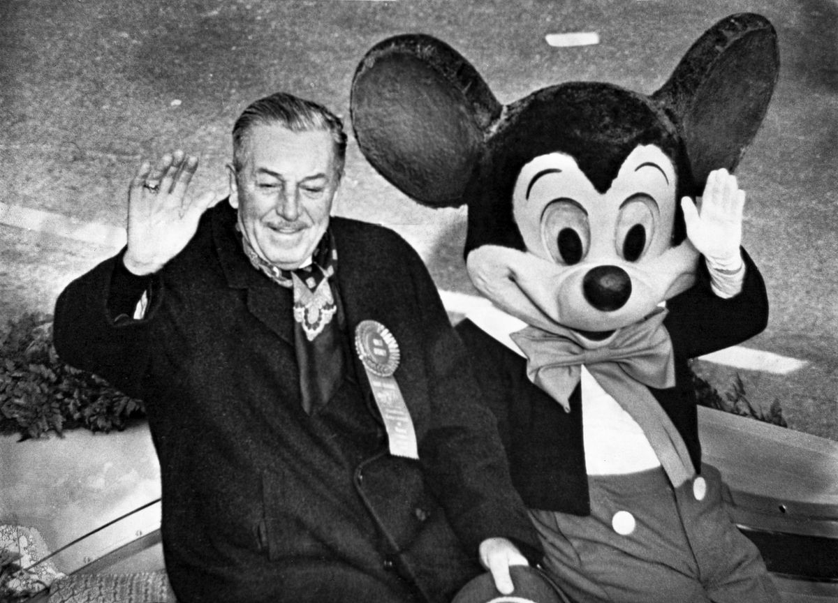 Une photo de stock de Walt Disney assis à côté d'un artiste costumé en tant que Mickey Mouse en 1966 en tant que grand maréchal de la parade des roses, les deux saluant le public