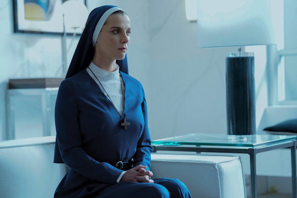 Simone (Betty Gilpin) assise sur un canapé dans son habit de nonne