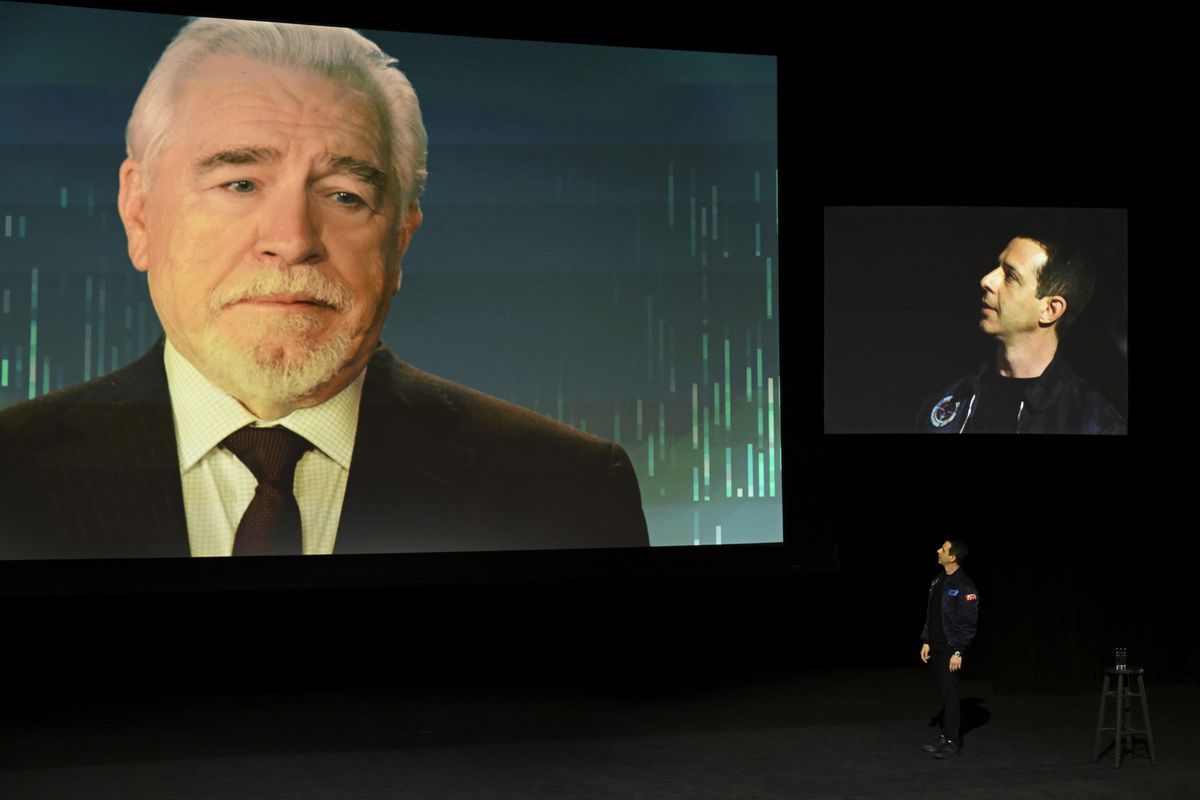 Logan Roy (Brian Cox) regarde d'un écran projeté Kendall (Jeremy Strong), qui lève les yeux et lui parle sur scène dans une image fixe de Succession