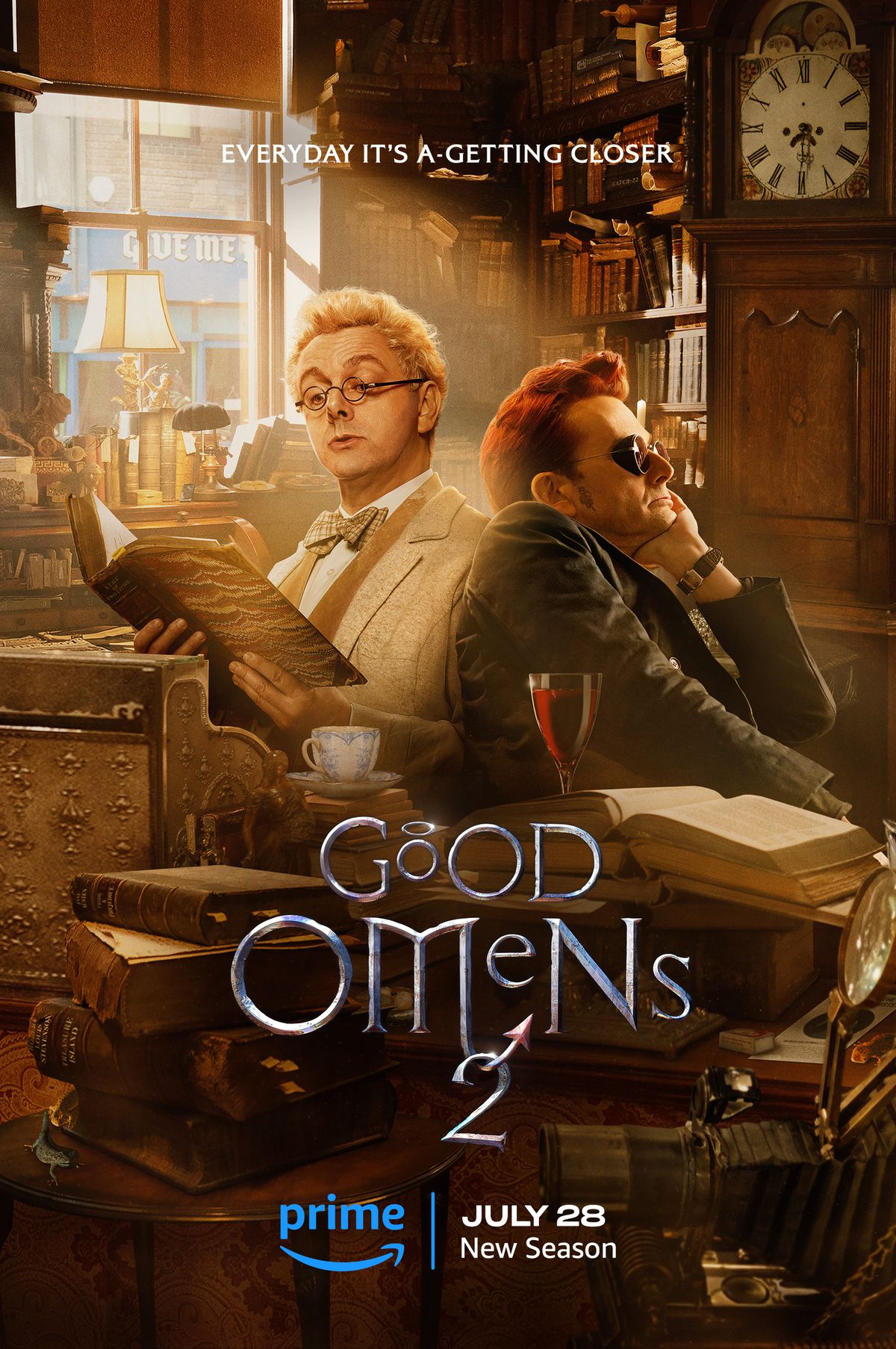 Michael Sheen dans le rôle d'Aziraphale et David Tennant dans celui de Crowley, tous deux allongés dans une librairie encombrée aux teintes dorées. 