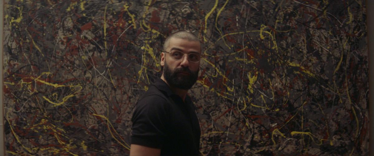 Oscar Isaac, avec des cheveux bourdonnants, des lunettes et une barbe pleine, se tient devant un mur peint (à la Jackson Pollack) dans Ex Machina.