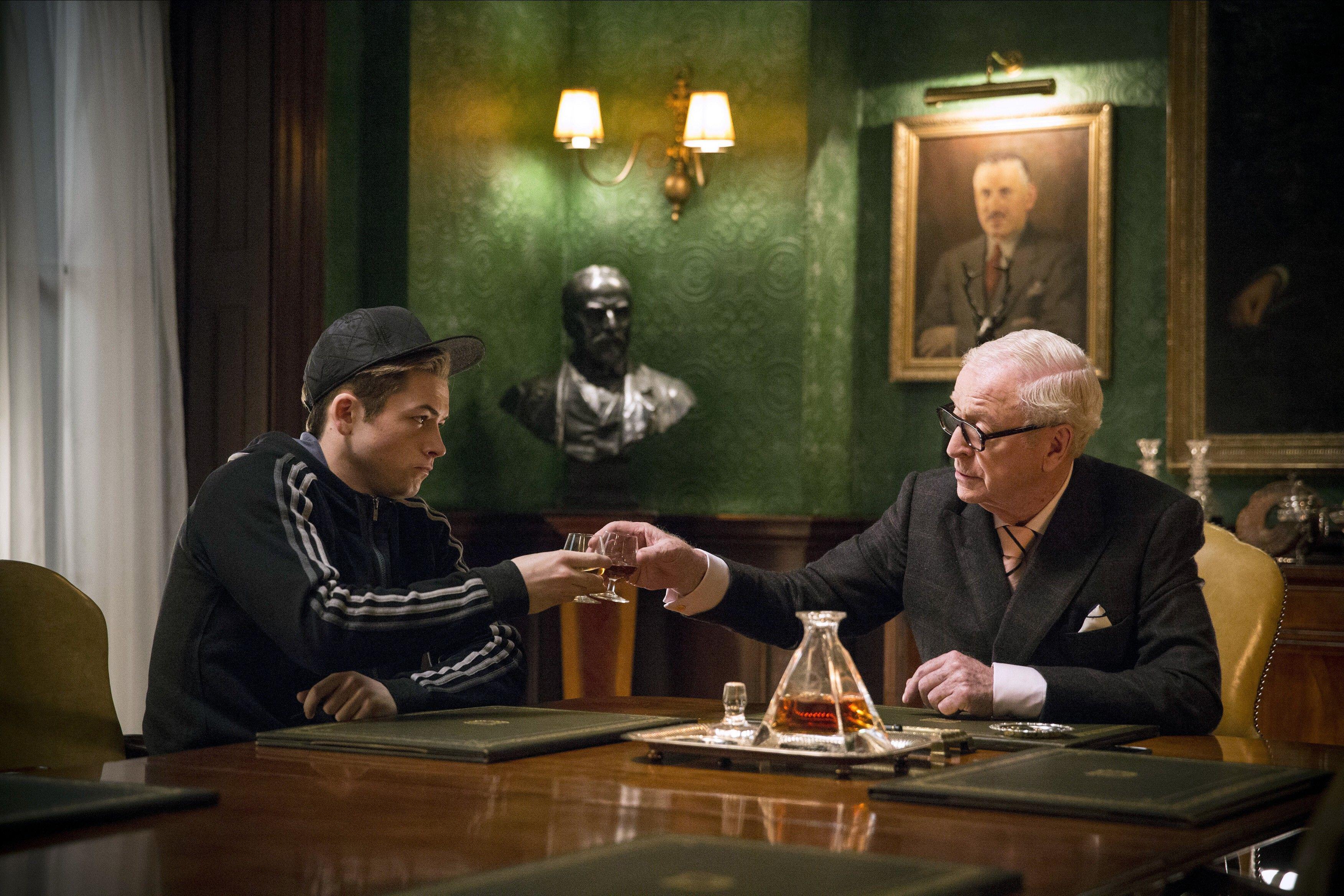 (L, R) Taron Egerton dans le rôle d'Eggsy, levant un verre à Michael Caine dans le rôle de Chester King dans Kingsman: The Secret Service