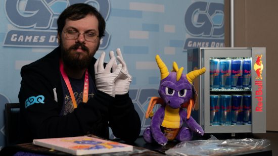 SGDQ 2023 - une personne portant des gants blancs croise ses doigts, tandis qu'une peluche Spyro le Dragon est assise à proximité.