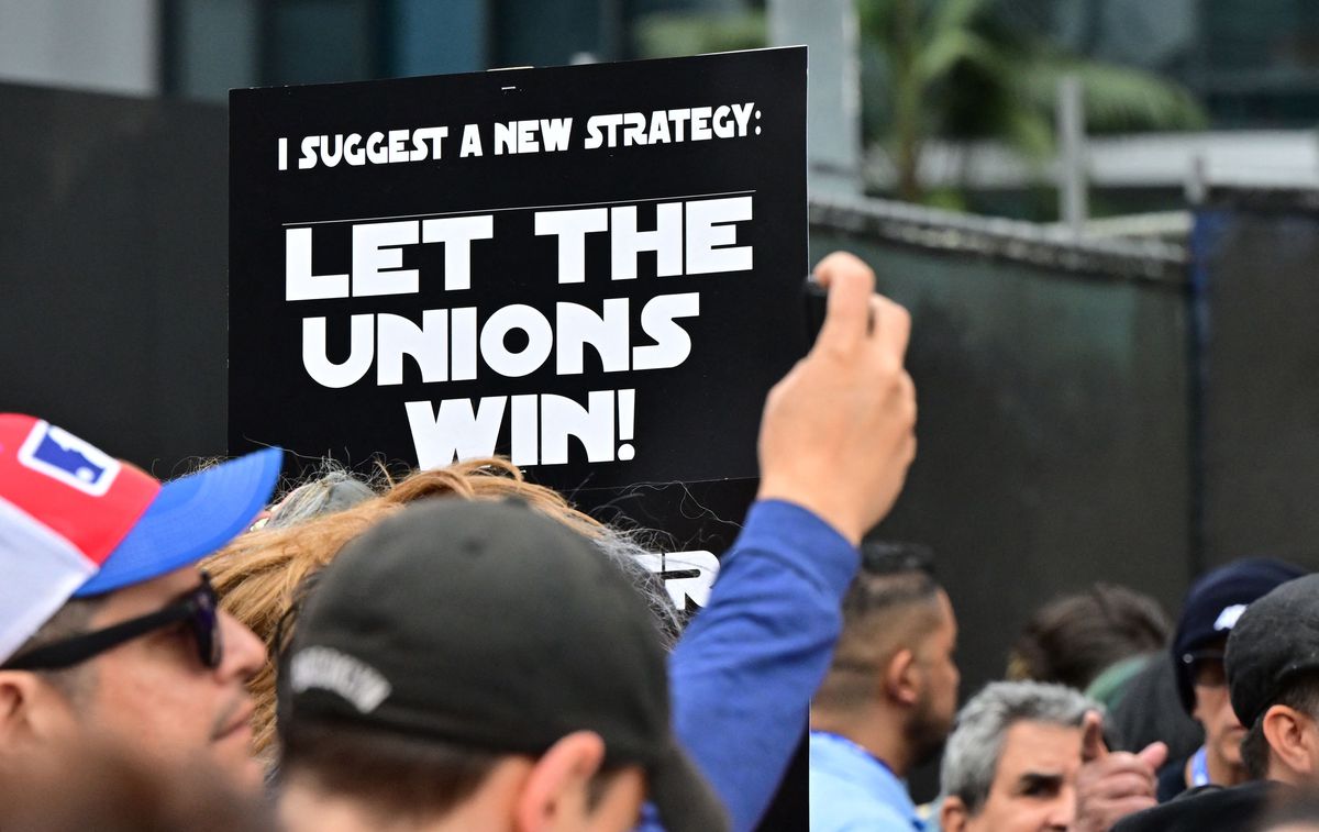 Des manifestants tiennent des pancartes pendant le piquetage pendant la grève continue de la Writers Guild of America (WGA) à Los Angeles, Californie, le 26 mai 2023. Au centre de l'image se trouve un signe dans la police du titre Star Wars qui dit 