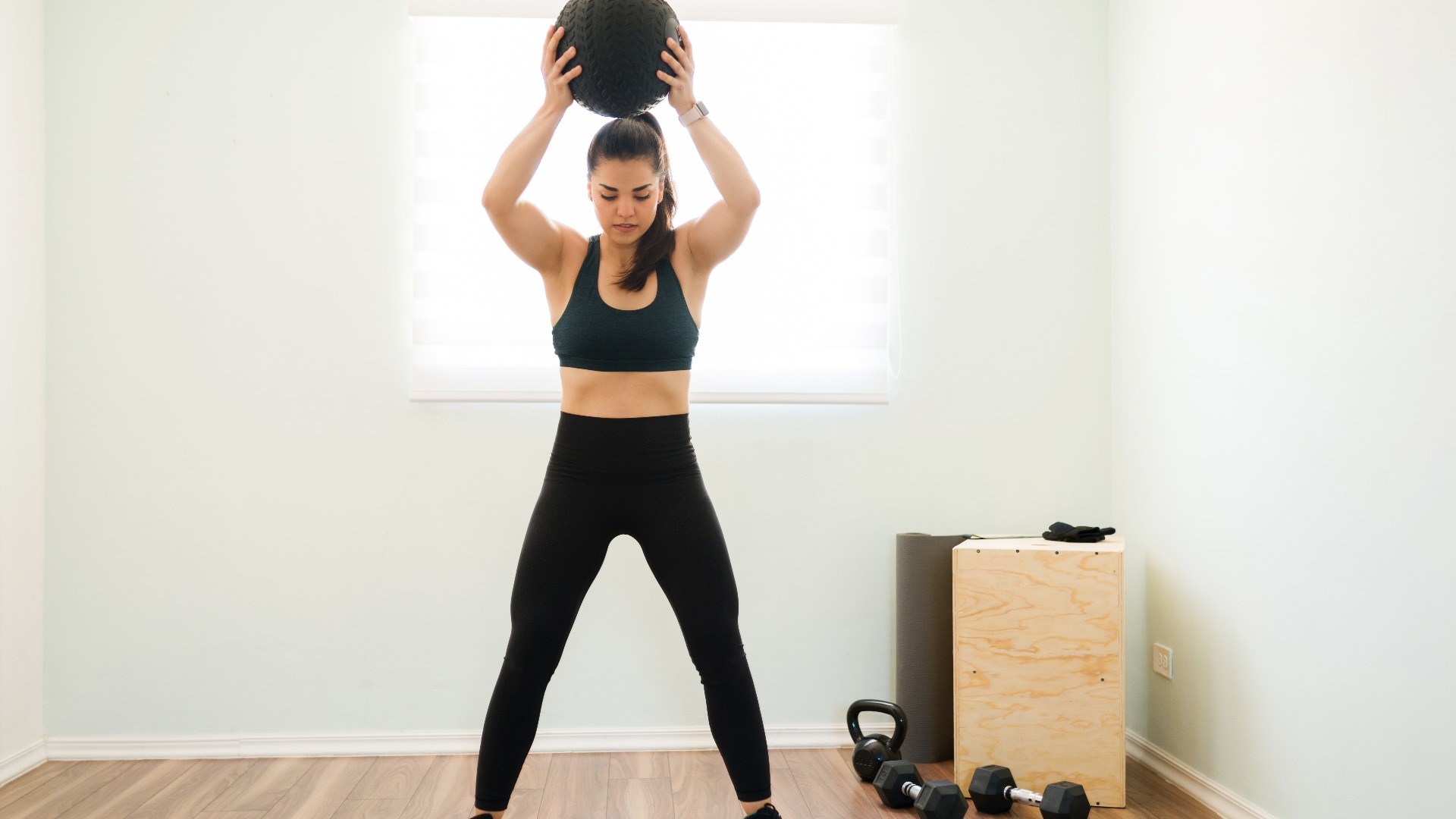 Femme dans une salle de sport à domicile lançant une balle au-dessus de sa tête lors d'un med ball slam