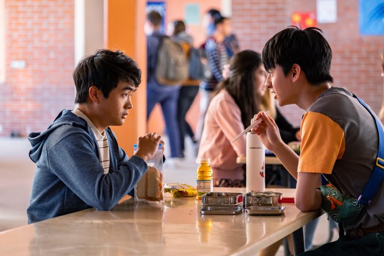 Two teenage boys sit across from each other at a cafeteria table; still from "American Born Chinese"