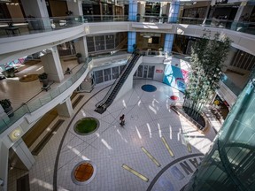 Un homme transporte des sacs d'épicerie en marchant dans une métropole déserte au centre commercial Metrotown à Burnaby, en Colombie-Britannique, le dimanche 12 avril 2020.