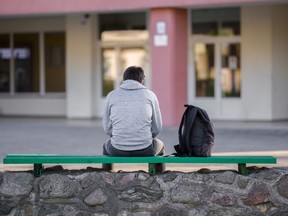 Un adolescent assis sur un banc à l'extérieur d'une école.