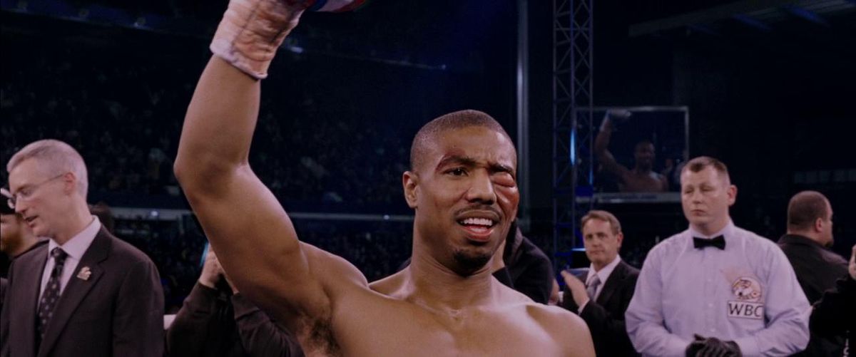 Michael B. Jordan dans le rôle d'Adonis Creed levant le poing et souriant avec un œil gauche enflé dans Creed.