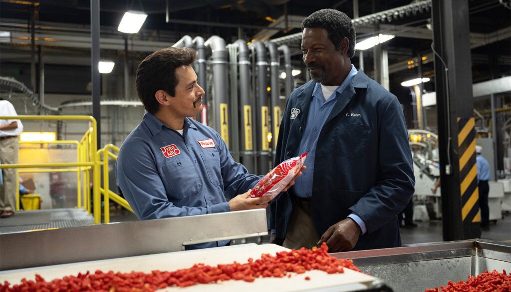 (LR) Jesse Garcia et Dennis Haysbert tenant un sac de Flamin' Hot Cheetos devant une usine de Cheetos à Flamin' Hot.